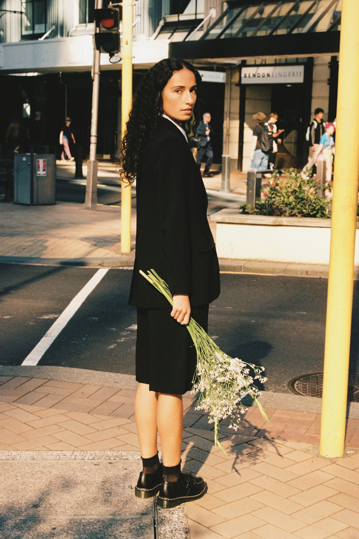 Woman in a black coat and shorts holding flowers on a city street
