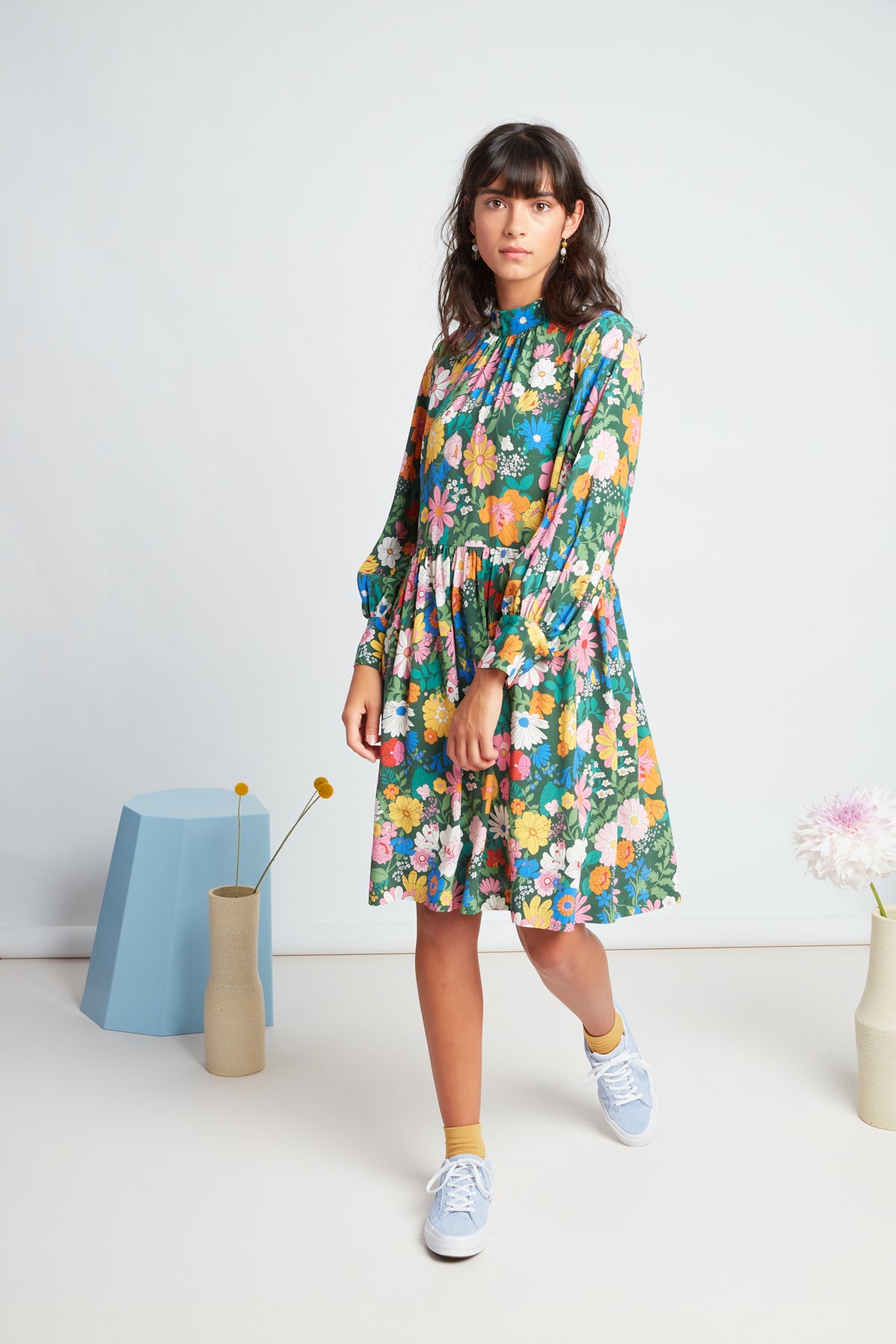 Clover dress by twenty-seven names. An elegant long-sleeved dress with a high-neck panel, waist ties, and gathers at the neck, cuff and skirt. Custom Botanical print, multi colour on a green base.