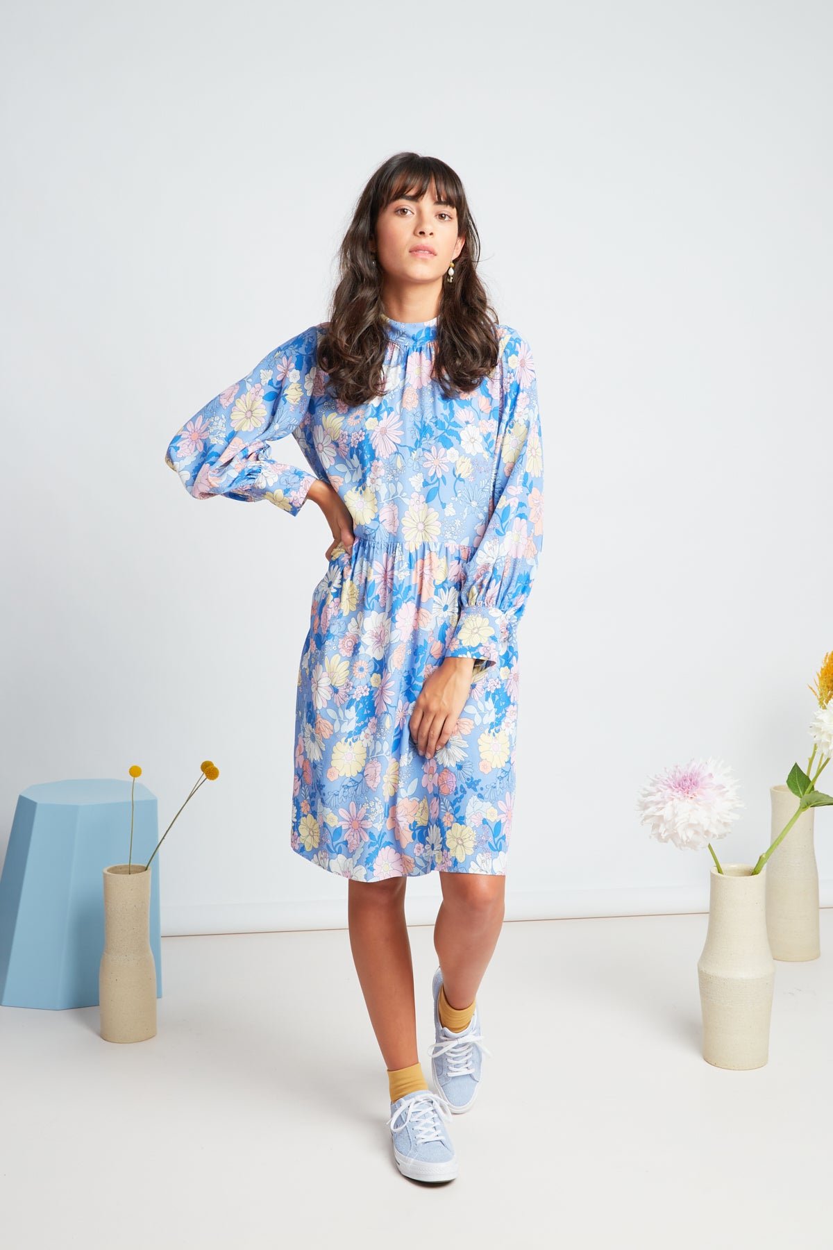 Clover dress by twenty-seven names. An elegant long-sleeved dress with a high-neck panel, waist ties, and gathers at the neck, cuff and skirt. Custom Botanical print, multi pastel colours on a Periwinkle blue base.
